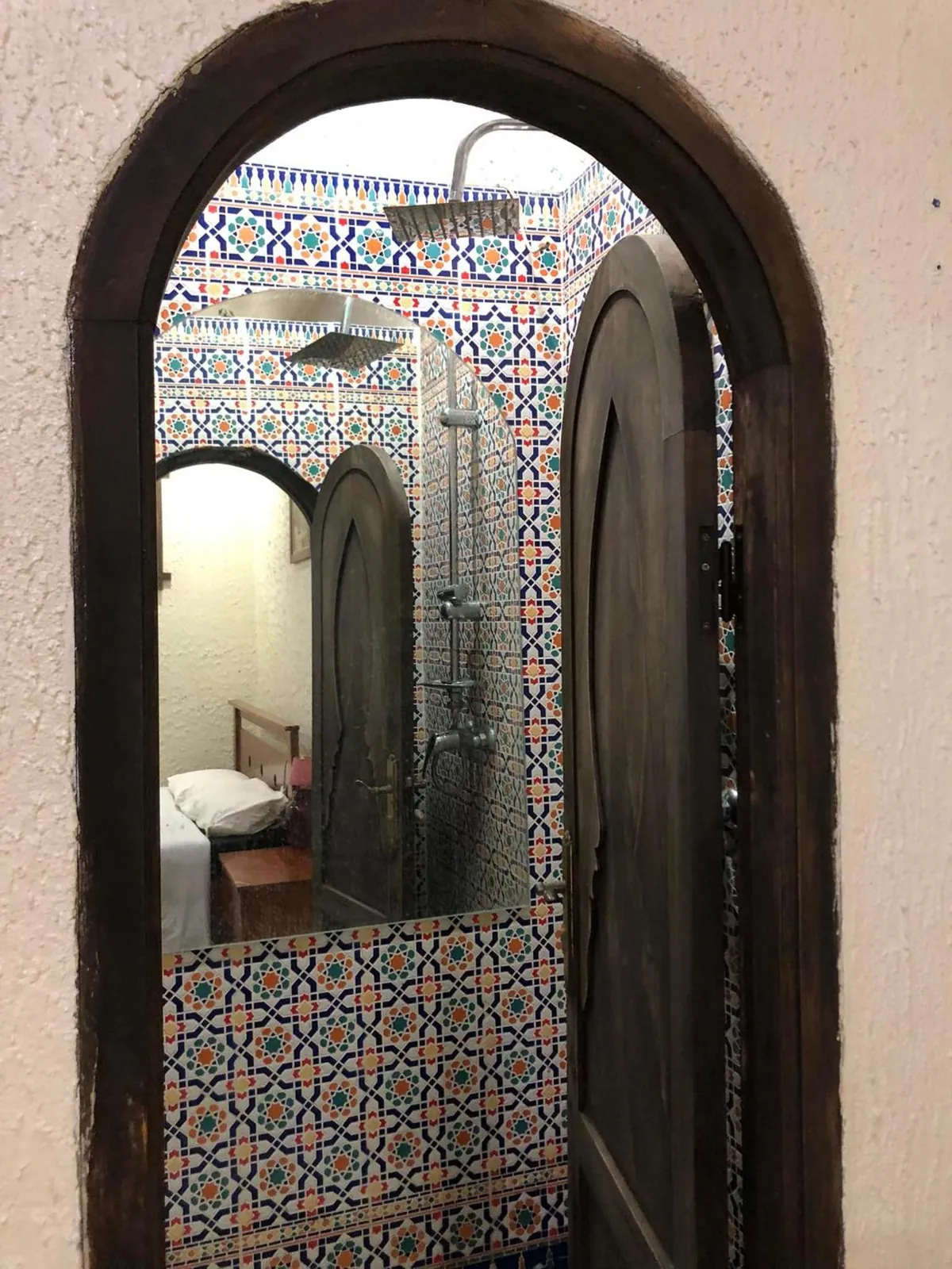 Une douche en zellige derrière un arc, et un lit