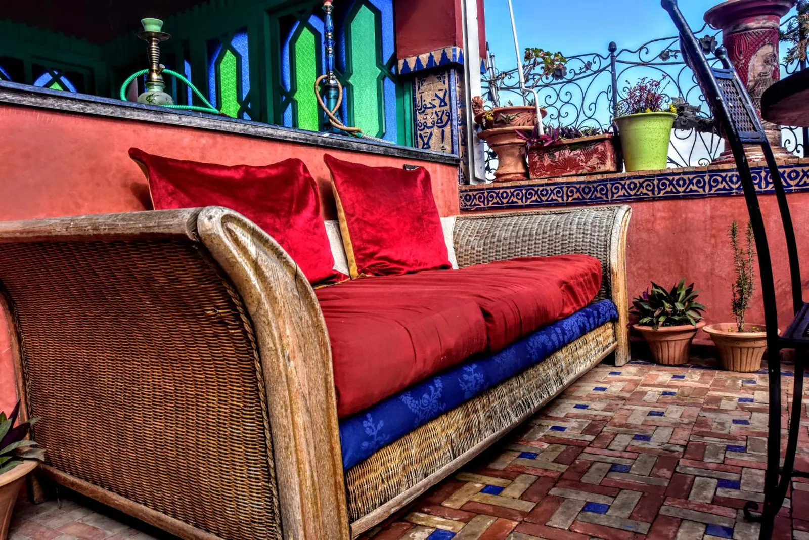Une banquette en osier et ses coussins rouges sur la terrasse