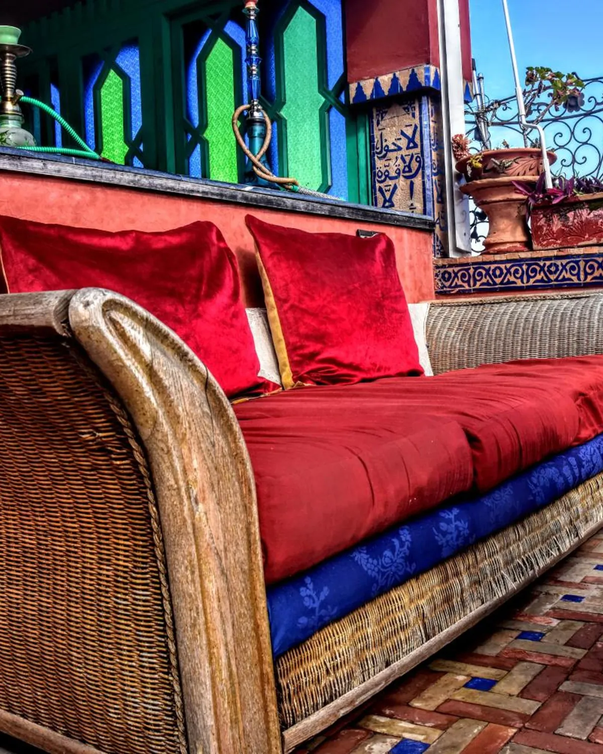 Une banquette en osier et ses coussins rouges sur la terrasse