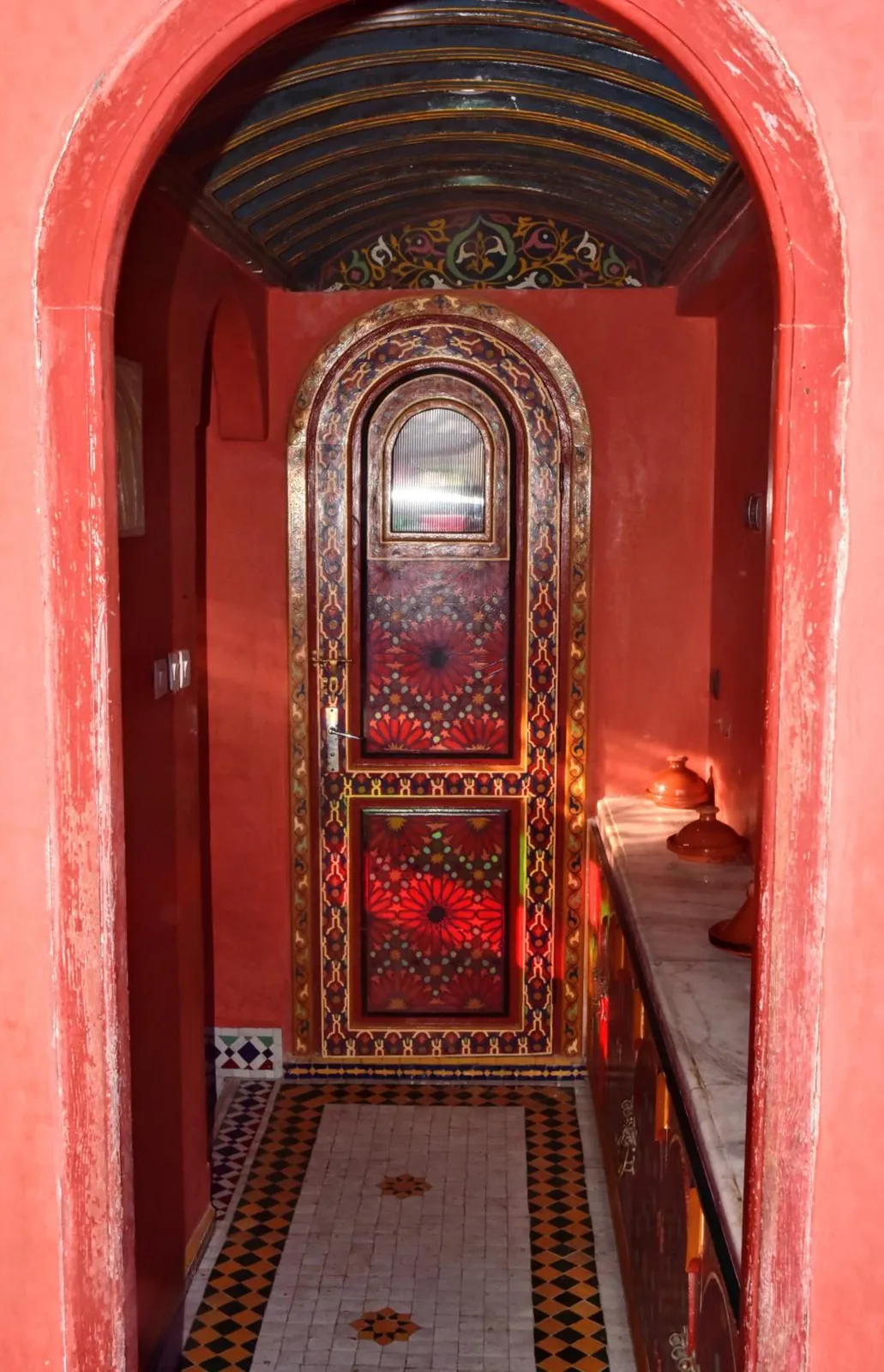 Un couloir rouge et sa porte en verre peint