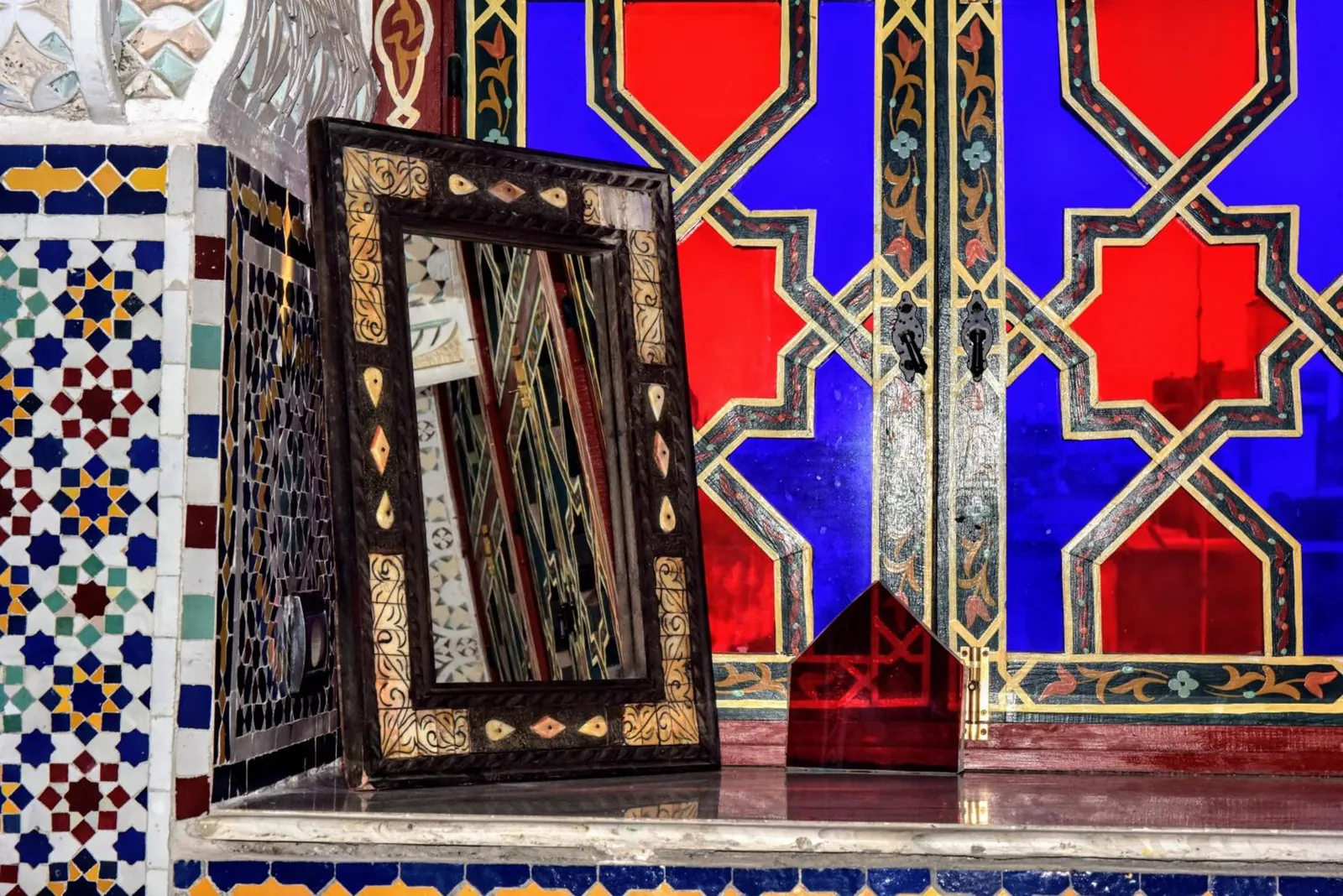 Un miroir sculpté devant un vitrail rouge et bleu